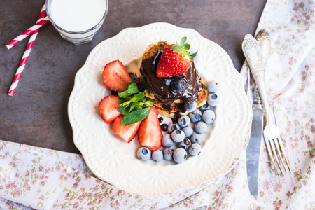 Pancakes with melted chocolate, strawberries, blueberries on a white plateの写真素材