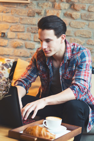Young man sitting at a cafe, using a laptop, drinking espressoの写真素材