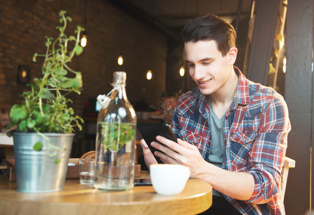 Young man sitting at a cafe, using a tablet, drinking espressoの写真素材