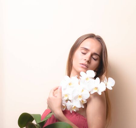 Portrait of a beautiful girl with an orchid on a light background.の写真素材