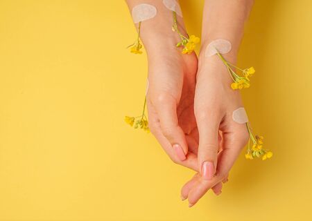 Hands art flower natural cosmetics women, yellow beautiful, spring flowers hand with bright contrast makeup, hand care. Fashion, creative beauty photo girl sitting at table,  yellow contrasting background.View from above, closeup.の写真素材