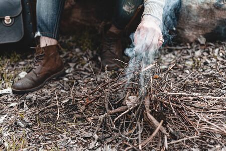 A stock photo of a man in nature sitting by a small fire, warming himself.の写真素材