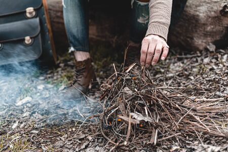 A stock photo of a man in nature sitting by a small fire, warming himself.の写真素材