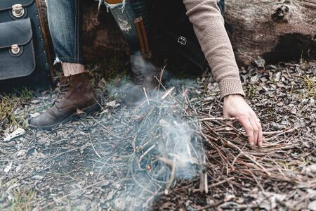 A stock photo of a man in nature sitting by a small fire, warming himself.の写真素材