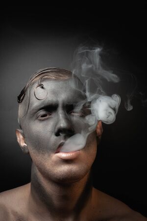 Close-up portrait of a handsome guy in makeup blows smoke. Stock art photo of a smoker.の写真素材