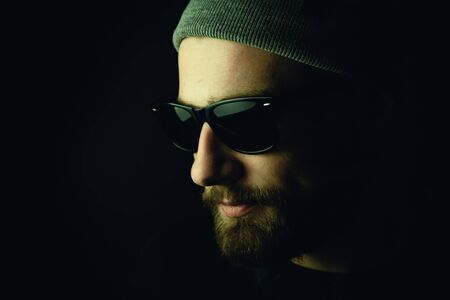 Portrait of a bearded, white hipster smoker on a dark background. Studio stock photo concept of...