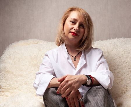 Portrait of an attractive middle-aged woman. Homemade portrait on the couch, middle-aged blonde.の写真素材