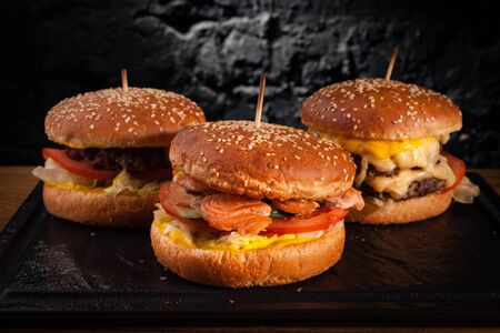 Menu of different burgers on one board. Side view of a fish burger, hamburger and cheese burger, against a wall background.の写真素材
