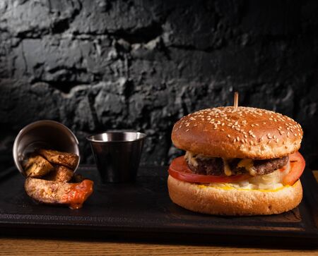 Burger and rustic potatoes on a wooden table on a stand. Against the background of a black wall.の写真素材