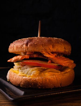 Appetizing fish burger with pieces of red fish meat on a brick wall background. Stock photo burger with fish filling.の写真素材