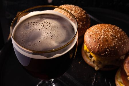 Cold beer in a glass and a snack in the form of juicy large burgers. Fast food.の写真素材