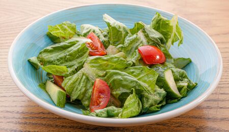 Simple healthy salad with leaf, tomato and cucumber in a plate on a wooden table.の写真素材