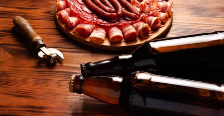 Beer snack in the form of meat products and bottled beer. Appetizer in the form of slicing bacon, salami, ham, hunting sausages. Stock photo beer and snack on a wooden table.の写真素材