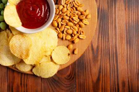 Assorted dry snacks on a wooden board. Chips, peanuts, croutons, wasabi.の写真素材