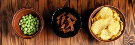 Assorted dry snacks on a wooden board. Chips, peanuts, croutons, wasabi.の写真素材