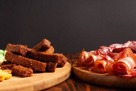 Assorted beer snacks on a wooden table with copy space. Sausage, ham, bacon. Salty snack chips, croutons, peanuts, wasabi nuts.の写真素材