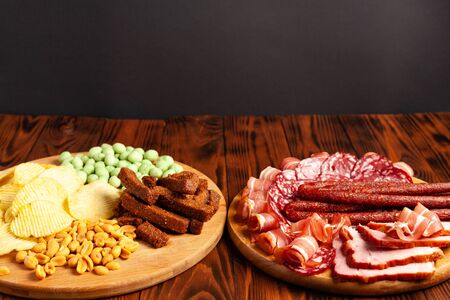 Assorted beer snacks on a wooden table with copy space. Sausage, ham, bacon. Salty snack chips, croutons, peanuts, wasabi nuts.の写真素材