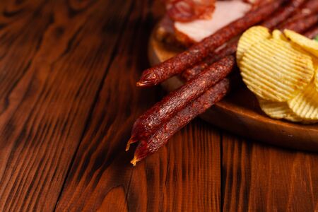 Assorted beer snacks on a wooden table with copy space. Sausage, ham, bacon. Salty snack chips, croutons, peanuts, wasabi nuts.の写真素材