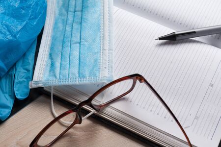 Empty notepad on hospital desk surrounded by medical equipment. Top view, flat lay composition. Notepad, mask, sanitizer and pen on table. Concept of virus 2019-nCoV, coronavirus, illness. Medical check up.の写真素材