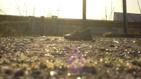 An old boot in the midst of urban trash, lie on the pavement under the rays of a sunny day.