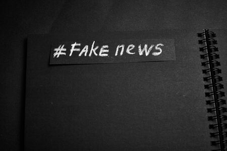 Fake news. The name is written in white chalk on a black background in the form of paper.の写真素材