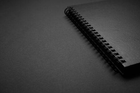 Blank black notebook on a black table, mockup photo. Blank black cover template with copy space for design. Black on black, minimal design concept.の写真素材