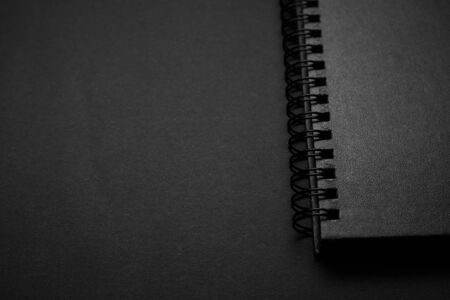 Blank black notebook on a black table, mockup photo. Blank black cover template with copy space for design. Black on black, minimal design concept.の写真素材