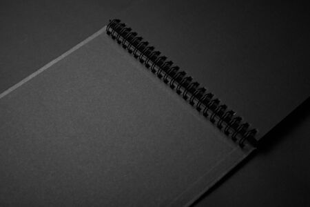 Blank black notebook on a black table, mockup photo. Blank black cover template with copy space for design. Black on black, minimal design concept.の写真素材