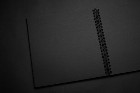 Blank black notebook on a black table, mockup photo. Blank black cover template with copy space for design. Black on black, minimal design concept.の写真素材