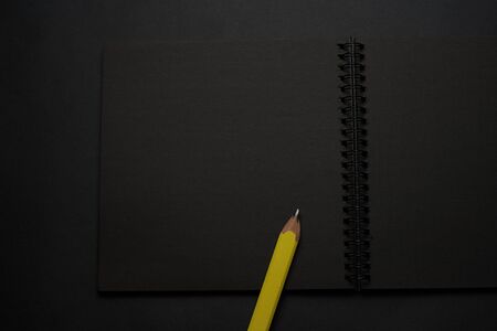 Blank black notebook on a black table, mockup photo. Blank black cover template with copy space for design. Black on black, minimal design concept.の写真素材