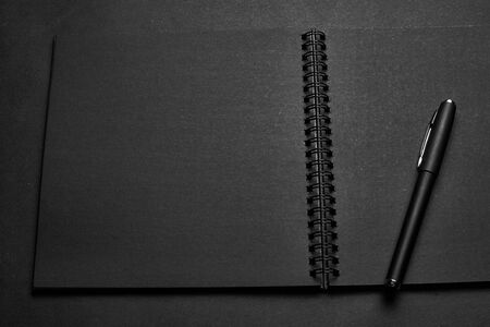 Blank black notebook on a black table, mockup photo. Blank black cover template with copy space for design. Black on black, minimal design concept.の写真素材