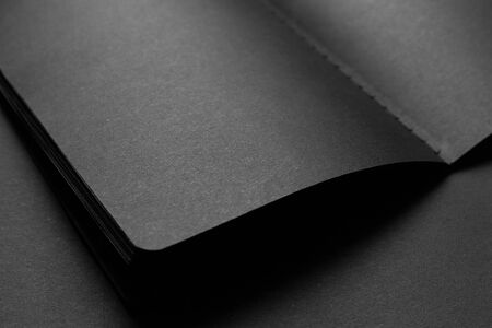 Blank black notebook on a black table, mockup photo. Blank black cover template with copy space for design. Black on black, minimal design concept.の写真素材