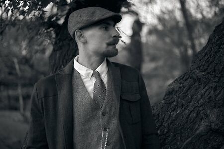 Retro 1920s portrait of an English gangster with a flat cap. Smokes a cigarette on the street..の写真素材