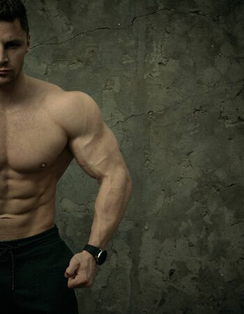 Handsome muscular man posing on concrete wall background. The concept of fitness, bodybuilding, health, lifestyle. Portrait of fitness fitness model.の写真素材
