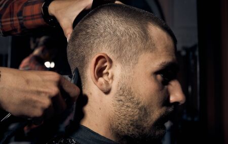 Barber cuts a guy at the hairdresser. Short haircut and alignment of hair contours. Close up portrait of a customer. Hair care.の写真素材