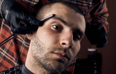 Barber cuts a guy at the hairdresser. Short haircut and alignment of hair contours. Close up portrait of a customer. Hair care.の写真素材