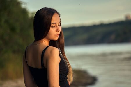Beautiful girl on the nature near the green shore. Enjoys the setting sun. The concept of outdoor recreation, a walk in the park. Relaxation from the bustle of the city.の写真素材