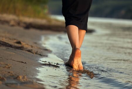 Female feet barefoot on a sandy beach in the water. Close-up of beautiful female legs. Wet foot.の写真素材