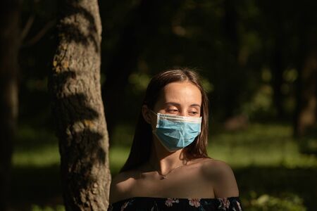 Girl resting in the park on a sunny summer day. Portrait of a woman taking off her face mask.の写真素材