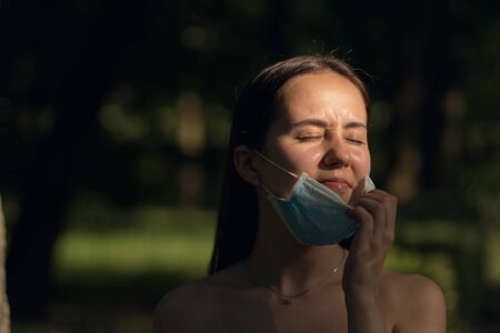 Girl resting in the park on a sunny summer day. Portrait of a woman taking off her face mask.の写真素材
