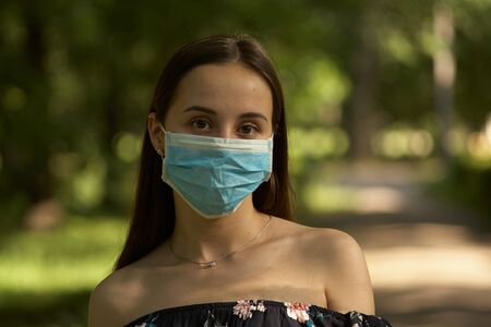 Girl resting in the park on a sunny summer day. Portrait of a woman taking off her face mask.の写真素材