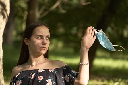 Girl resting in the park on a sunny summer day. Portrait of a woman taking off her face mask.の写真素材
