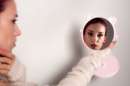 A makeup girl is looking in a round mirror.の写真素材
