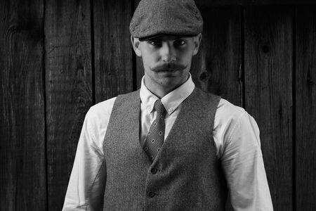 Retro portrait of a guy with a mustache in a shirt, vest and tie with a cap.