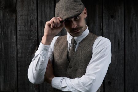 Retro portrait of a guy with a mustache in a shirt, vest and tie with a cap.