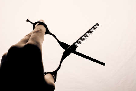 Scissors in the hand of the hairdresser silhouette on a light background.