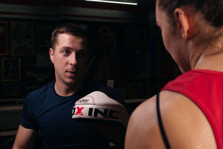UKRAINE, ZAPOROZHYE - March 11, 2020: Boxing coach holds boxing paws. Training, self defense. Boxing training with a girl.のeditorial素材