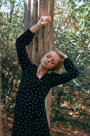 Fashionable portrait of a girl in a dress with polka dots on a background of nature and old...