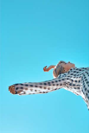 Cute fashionable girl in a plaid dress posing against the blue sky.の写真素材