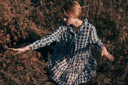 Attractive girl resting in the yellow dry grass in a dress barefoot. Model in a plaid dress.の写真素材